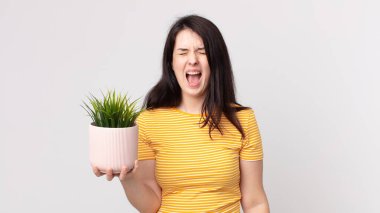 Güzel bir kadın agresif bir şekilde bağırıyor, kızgın görünüyor ve elinde dekoratif bir bitki tutuyor.