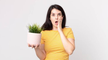 Güzel bir kadın şok olmuş, korkmuş ve elinde dekoratif bir bitki tutuyor.