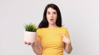 Şok olmuş ve ağzı açık, kendini gösteren ve elinde dekoratif bir bitki tutan güzel bir kadın.
