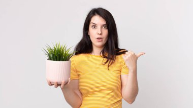 Güzel bir kadın inançsızlıktan şaşkına dönmüş ve elinde dekoratif bir bitki tutuyor.