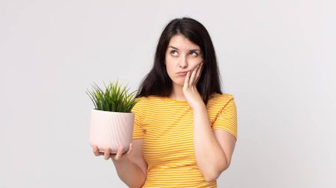 Güzel bir kadın sıkılıyor, hayal kırıklığına uğruyor ve uykulu. Yorucu bir günün ardından elinde dekoratif bir bitki tutuyor.