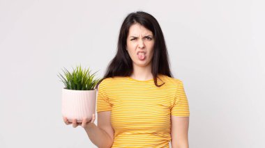 Güzel bir kadın midesi bulanmış ve rahatsız olmuş hissediyor. Dilini çıkarmış ve elinde dekoratif bir bitki tutuyor.