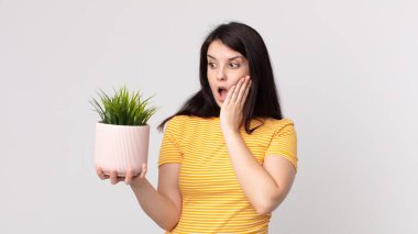 Güzel bir kadın mutlu, heyecanlı ve şaşırmış ve elinde dekoratif bir bitki tutuyor.