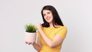 Güzel bir kadın kendini mutlu hisseder ve bir meydan okumayla yüzleşir ya da kutlama yapar ve elinde dekoratif bir bitki tutar.