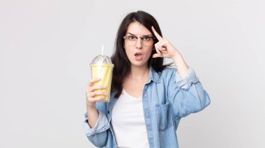 Güzel kadın şaşırmış görünüyor, yeni bir düşünce, fikir ya da konsept fark ediyor ve elinde vanilyalı milkshake tutuyor.