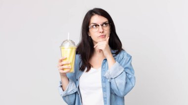 Güzel bir kadın düşünüyor, kuşkulu ve şaşkın hissediyor ve elinde vanilyalı milkshake tutuyor.