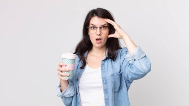 Güzel bir kadın mutlu görünüyor, şaşırmış ve şaşırmış ve elinde kahve tutuyor.