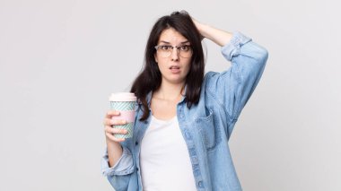 Güzel bir kadın kendini stresli, endişeli ya da korkmuş hissediyor. Elleri başının üstünde ve elinde kahve tutuyor.