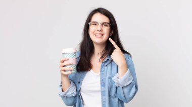 Güzel bir kadın, kendine güvenerek gülümsüyor, kendi gülüşünü gösteriyor ve elinde kahve tutuyor.
