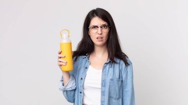 Güzel kadın şaşkın ve kafası karışmış hissediyor ve elinde kahve termosu tutuyor