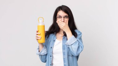 Güzel bir kadın elleri ile ağzını kapatıyor ve elinde kahve termosu tutuyor.