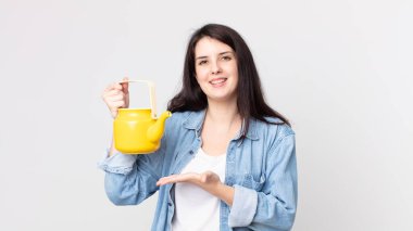 Güzel bir kadın neşeyle gülümsüyor, mutlu hissediyor ve bir konsept gösteriyor ve bir çaydanlık tutuyor.