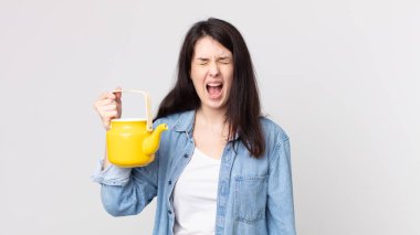 Güzel bir kadın agresif bir şekilde bağırıyor, kızgın görünüyor ve elinde çaydanlık tutuyor.