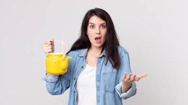 Güzel bir kadın inanılmaz bir sürprizle şaşkın, şaşkın ve hayretler içinde elinde bir çaydanlık tutuyor.
