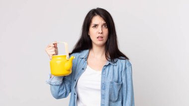Güzel bir kadın şaşkın, kafası karışmış ve elinde çaydanlık tutuyor.