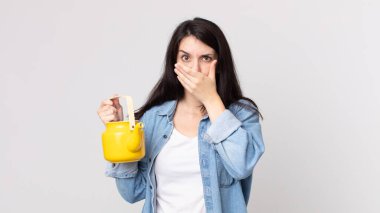 Güzel bir kadın elleri ile ağzını kapatıyor ve elinde bir çaydanlık tutuyor.