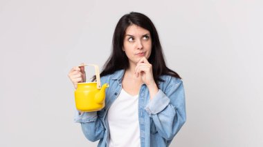 Düşünen, kuşkulu, kafası karışık ve elinde çaydanlık tutan güzel bir kadın.