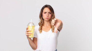 Oldukça zayıf bir kadın kendini kötü hissediyor, baş parmaklarını gösteriyor ve elinde vanilyalı milkshake tutuyor.