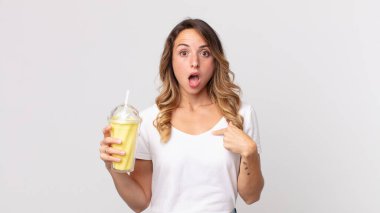 Oldukça zayıf görünen bir kadın ağzı açık, elinde vanilyalı milkshake tutarak ve kendini göstererek şok olmuş ve şaşırmış görünüyor.