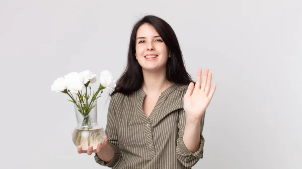 笑顔で手を振って歓迎し挨拶し装飾的な花を持ってる ヘッドセットを装着したアシスタントエージェント — ストック写真