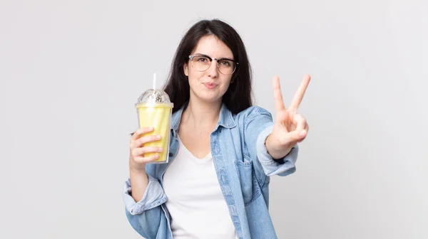 Bonita Mulher Sorrindo Olhando Amigável Mostrando Número Dois Segurando Milkshake — Fotografia de Stock