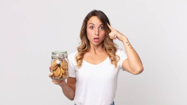 Oldukça zayıf bir kadın şaşırmış görünüyor, yeni bir düşünce, fikir ya da konsept fark ediyor ve elinde cam bir kurabiye şişesi tutuyor.