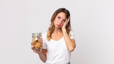 Oldukça zayıf bir kadın sıkılmış, hayal kırıklığına uğramış ve uykulu bir halde yorucu bir günün ardından elinde cam bir kurabiye şişesi tutuyor.