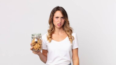 Kafası karışmış, kafası karışmış ve elinde cam bir kurabiye şişesi tutan oldukça zayıf bir kadın.