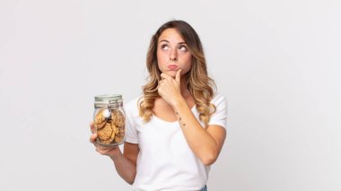 Oldukça ince düşünen, kuşkulu, kafası karışık ve elinde cam bir kurabiye şişesi tutan bir kadın.