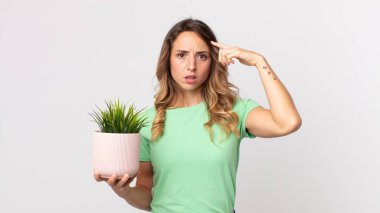 Kafası karışmış, kafası karışmış, deli olduğunu ve elinde dekoratif bir bitki tuttuğunu gösteren ince bir kadın.