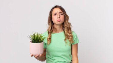 Oldukça zayıf bir kadın üzgün ve mızmızlanıyor. Mutsuz bir bakışla, ağlıyor ve elinde dekoratif bir bitki tutuyor.