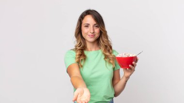 Oldukça zayıf bir kadın mutlu bir şekilde gülümsüyor ve bir konsept sunuyor ve elinde bir kahvaltı kasesi tutuyor.