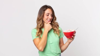 Gülümseyen, güler yüzlü, kendine güveni tam, eli çenesinde ve elinde kahvaltı kasesi olan zayıf bir kadın.