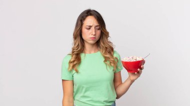 Oldukça zayıf bir kadın üzgün, üzgün ya da kızgın ve yana bakıyor ve elinde kahvaltı kasesi tutuyor.