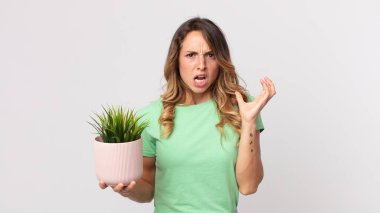 Elleri havada ve elinde dekoratif bir bitki tutarak çığlık atan oldukça zayıf bir kadın.