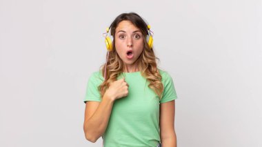 Oldukça zayıf bir kadın ağzı açık, şok olmuş ve şaşırmış görünüyor. Kulaklıkla kendini dinleyen müziğe işaret ediyor.