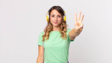 Oldukça zayıf bir kadın gülümsüyor ve arkadaş canlısı görünüyor, üç numara kulaklıkla müzik dinliyor.