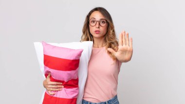 Oldukça zayıf bir kadın ciddi görünüyor. Avuç içini gösteriyor. Pijama giymeyi ve yastık tutmayı kesiyor.