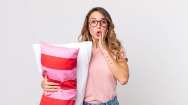 Oldukça zayıf bir kadın şok olmuş ve korkmuş hissediyor pijama giyiyor ve elinde yastık tutuyor.