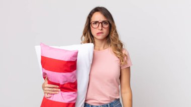 Kafası karışmış, pijama giymiş ve elinde yastıkla oldukça zayıf görünen bir kadın.