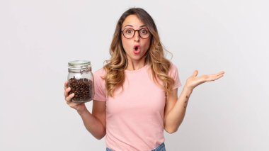 Oldukça zayıf bir kadın şaşırmış ve şok olmuş görünüyor, çenesi düşmüş, elinde bir nesne, elinde kahve şişesi tutuyor.