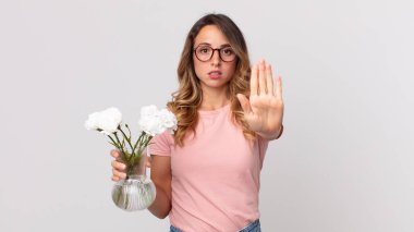 Oldukça zayıf bir kadın ciddi görünüyor. Avuç içi gösteriyor. Jesti durduruyor ve elinde süs çiçekleri tutuyor.