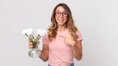 Oldukça zayıf bir kadın heyecanlı ve şaşırmış görünüyor. Yan tarafı gösteriyor ve elinde süs çiçekleri tutuyor.