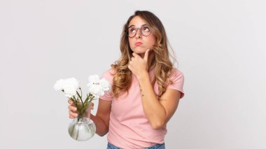 Oldukça ince düşünen, kuşkulu hisseden, kafası karışık ve elinde süslü çiçekler tutan bir kadın.