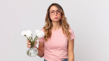 Oldukça zayıf bir kadın üzgün ve mızmız, mutsuz bir bakışla ağlıyor ve elinde dekoratif çiçekler tutuyor.