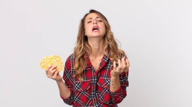 Oldukça zayıf bir kadın umutsuz, hayal kırıklığına uğramış ve stresli görünüyor ve elinde diyet pirinç keki tutuyor.