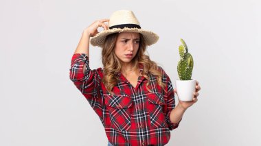 Kafası karışmış, kafası karışmış, kaktüs tutan ince bir kadın. çiftçi kavramı