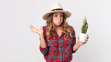 Kafası karışmış, kafası karışmış ve elinde kaktüs tutan oldukça zayıf bir kadın. çiftçi kavramı