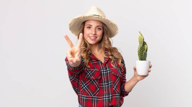 Gülümseyen ve mutlu görünen oldukça zayıf bir kadın. Zafer veya barış simgesi olarak kaktüs tutuyor. çiftçi kavramı