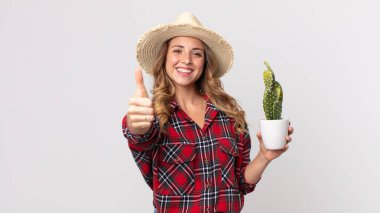 Oldukça zayıf bir kadın gururlu, parmakları havada bir kaktüsle gülümsüyor. çiftçi kavramı